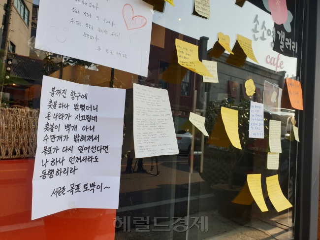 손혜원 의원의 부동산 투기 의혹이 불거진 전남 목포시 원도심 골목. 오후 6시임에도 불이 켜진 간판은 창성장이 거의 유일하다. 주민들은 외지인이 건물을 사들이고 방치해 원도심이 사실상 유령도시처럼 변했다고 했다(왼쪽). 원도심 내부에 버려진 일본식 건물. 인근 주민에 따르면 수년 전까지 주점으로 이용됐지만, 유동인구가 줄면서 폐업한 뒤 방치되고 있다(오른쪽 위). 문화재 구역 내에서 손 의원의 조카가 운영 중인 카페. 방문객과 인근 주민들이 붙여놓은 응원 메시지로 유리벽이 채워져있다.  [사진=유오상 기자]