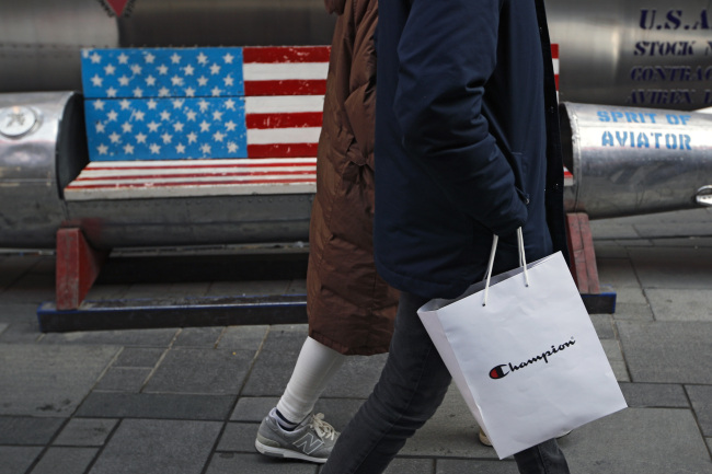 A couple carries a paper bag containing goods purchased from American brand Champion past a bench painted with the US flag at the capital city's popular shopping mall in Beijing, Wednesday, Feb. 13, 2019. (AP-Yonhap)