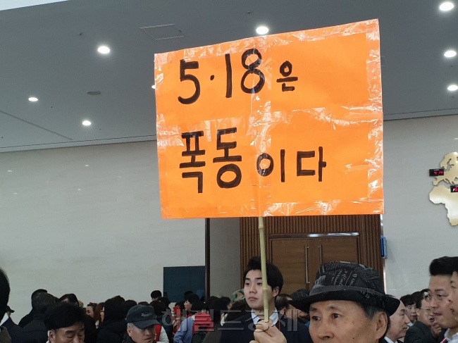 지난 21일 부산 벡스코에서 열린 자유한국당 전당대회 합동연설회에 참가한 한 지지자가 ‘5ㆍ18은 폭동이다’란 내용의 피켓을 들고 1인 시위를 하고 있다(왼쪽). 연설회장 앞에서 당 대표 후보인 황교안 전 국무총리 지지자들이 사물놀이를 하며 유세에 나서고 있다. 뒤에는 5ㆍ18 망언을 규탄하는 시민단체의 기자회견이 동시에 진행되고 있다.  [유오상 기자/osyoo@]