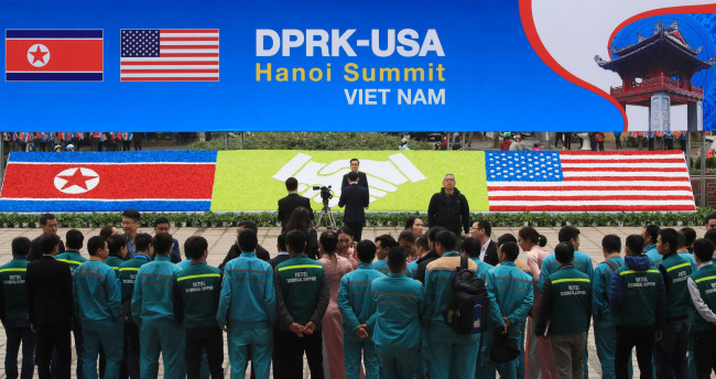 Vietnamese officials stand facing a sign installed for the US-North Korea summit in Hanoi on Sunday (Yonnhap)