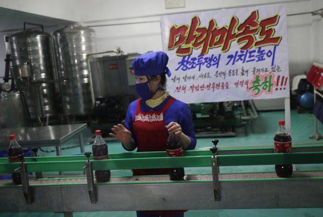 In this March 13, 2019, photo, a worker runs a conveyor belt moving bottles of soft drinks near a propaganda banner that reads "Let`s uphold the banner of the speed of Mallima (a mythical Pegasus-type horse)" at Kumkhop Trading Co. food factory in Pyongyang, North Korea. North Korean factories are filling city store shelves with ever better and fancier snack foods and sugary drinks, while government officials and international aid organizations warn the nation could be on the verge of a major food crisis. (AP Photo/Dita Alangkara)