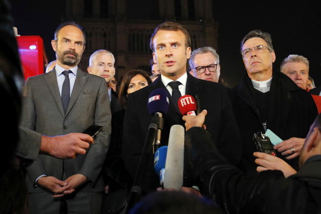 French President Emmanuel Macron speaks as Prime Minister Edouard Philippe and Archbishop of Paris, Michel Aupetit, stand near the Notre Dame Cathedral where a fire burns in Paris, France, 15 April 2019. (EPA=Yonhap)