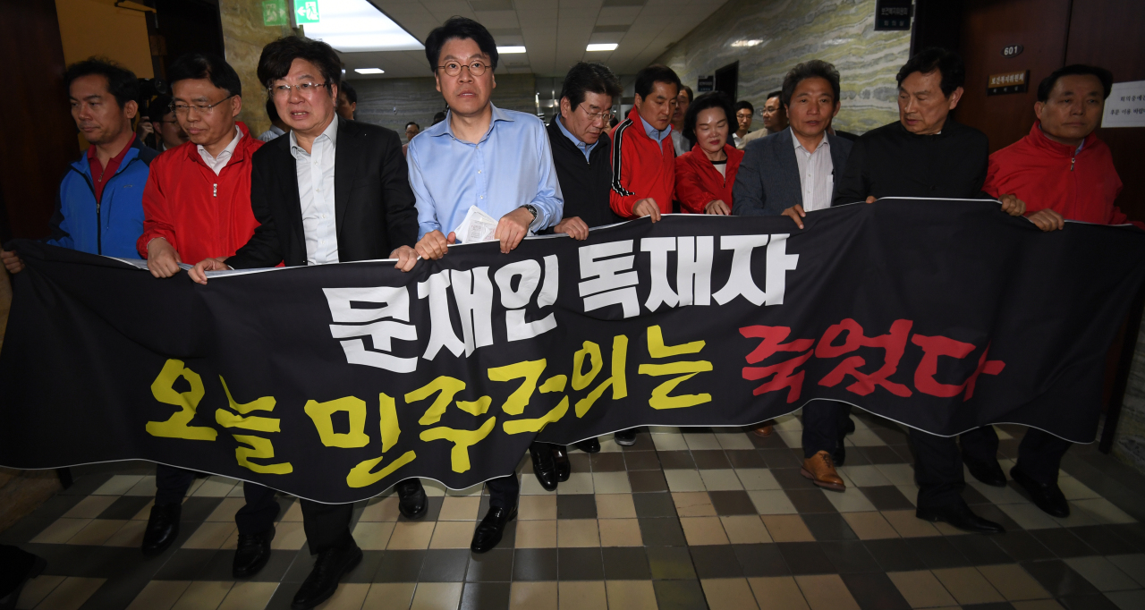 Liberty Korea Party lawmakers walk along a corridor at the National Assembly holding a banner that reads "Dictator Moon Jae-in, democracy died today," on Monday. Yonhap