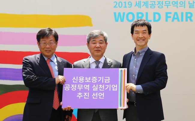 사진=조경식 신용보증기금 이사(가운데)가 김경민 한국공정무역협의회 대표이사(사진 왼쪽), 이강백 한국공정무역마을위원회 위원장과 함께 11일 서울숲에서 개최된 ‘2019년 세계 공정무역의 날 한국 페스티벌’에서 ‘공정무역 실천기업’ 추진을 선언하고 기념촬영을 하고 있다. [신용보증기금 제공]