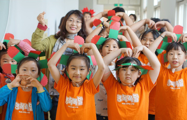 A teacher and students pose for a picture at an elementary school in Gunsan, North Jeolla Province, Wednesday. The students are wearing paper carnations and making hearts over their heads. (Hoehyeon Middle School/Yonhap)