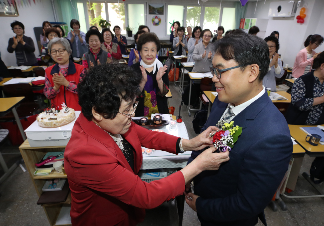 An elderly woman and lifelong learner attaches a corsage to her teacher’s jacket Wednesday in Mapo-gu, Seoul. (Yonhap)