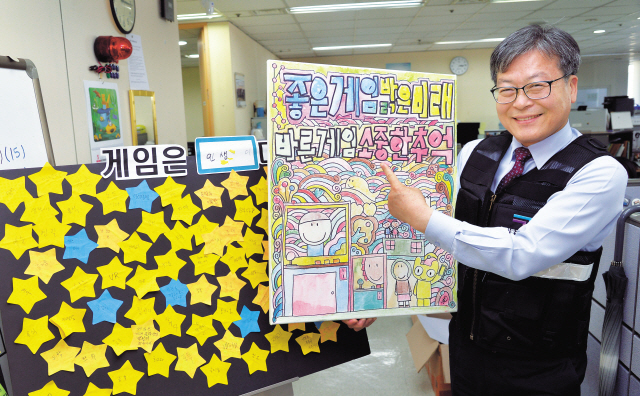 이재홍 게임물관리위원장은 독특한 이력을 가지고 있다. 국내에서 공대를 나와서 일본에서 종합문화연구를 공부한 후 다시 국내에서 국문학 박사를 취득했다. 게임교육원을 설립하고, 게임학회장을 비롯한 각종 관련 단체장을 수차례 역임했고, 문예창작과 교수로 강단에도 섰다. 그런 ‘하이브리드’한 경력 덕분에 이위원장이 게임의 진흥과 규제 사이에서 균형을 잘 잡을 것이라는 기대가 상당하다. 그는 “‘실감세대’들이 중심인 ‘혼합현실의 시대’가 곧 온다. 게임이 시대의 중심 산업이 될 것”이라고 했다. 이 위원장이 서울 사무소에서 좋은 게임 문화 조성 게시물을 들고 포즈를 취했다.  정희조 기자/checho@heraldcorp.com