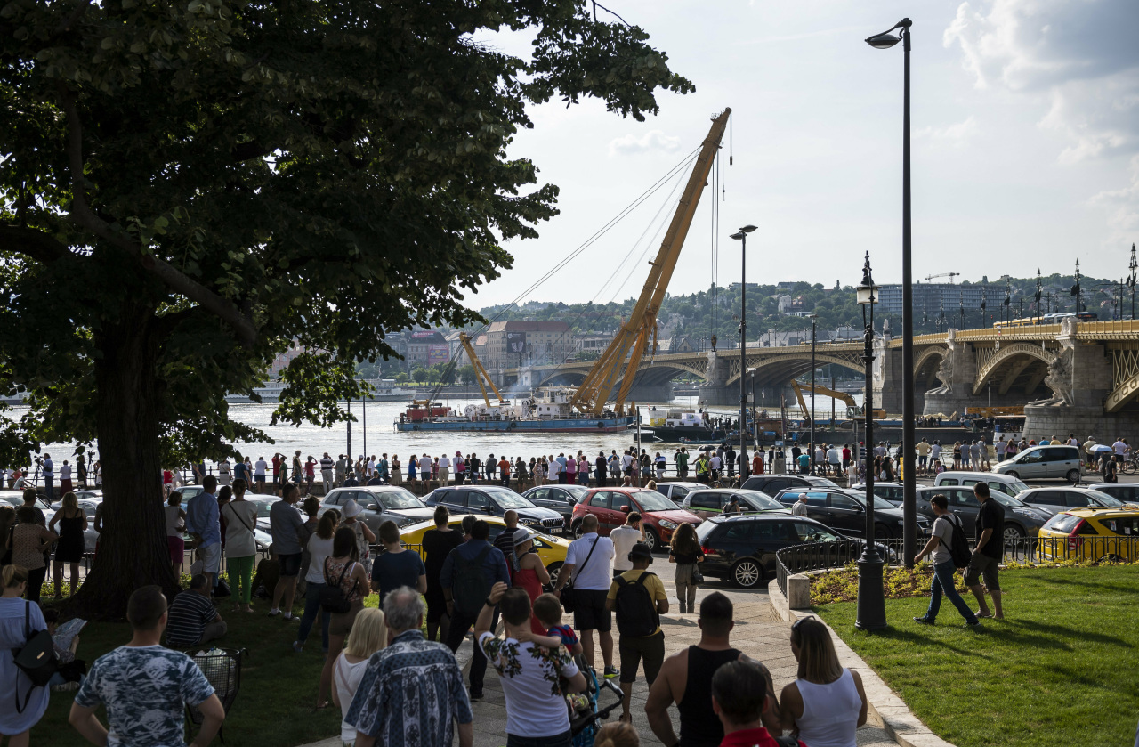 People gather on the banks of the Danube river to watch as a 200-ton lift capa city crane manoeuvres into position near the Margaret Bridge, preparing to lift the sunk shipwreck, from the scene of the deadly boat accident in Budapest, Hungary, Monday, June 10, 2019. (AP-Yonhap)