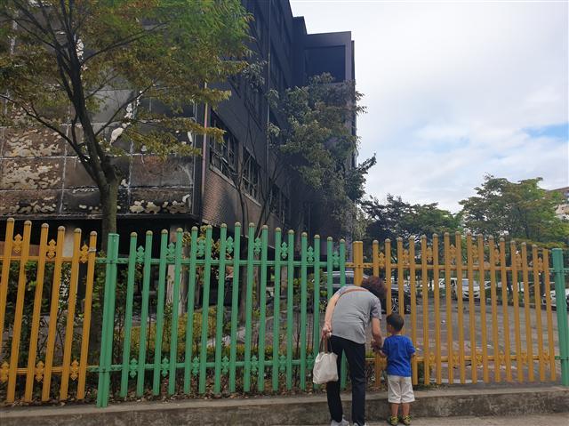 7일 오전 한 보호자가 아이와 함께 전날 대형화재로 불 탄 은명초등학교를 바라보고 있다. 은명초등학교는 27,28일 임시휴교했다. 오른쪽 사진은 전날 화재 모습.  김유진 기자/kacew@·[연합]