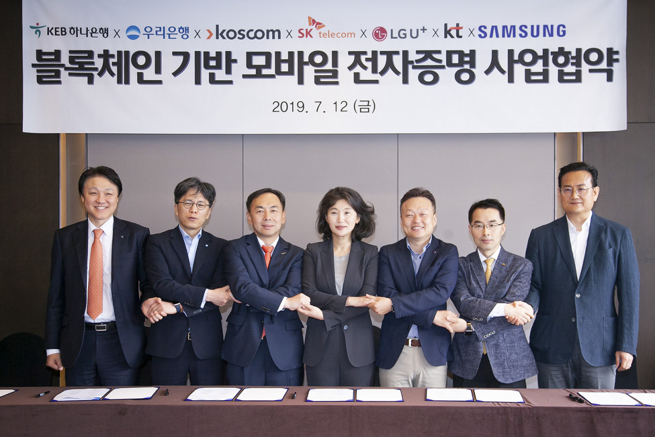 업무 협약식에 참석한 7개 참여사 관계자들이 기념촬영 하는 모습. 사진 왼쪽부터 KEB하나은행 미래금융그룹 한준성 부행장, 우리은행 디지털금융그룹장 황원철 상무, 코스콤 미래성장본부 김계영 본부장, SK텔레콤 블록체인 및 인증 유닛장 오세현 전무, LG유플러스 FC부문장 이상민 전무, KT 블록체인비즈센터장 서영일 상무, 삼성전자 서비스기획그룹장 김주완 상무 순 [SK텔레콤 제공]