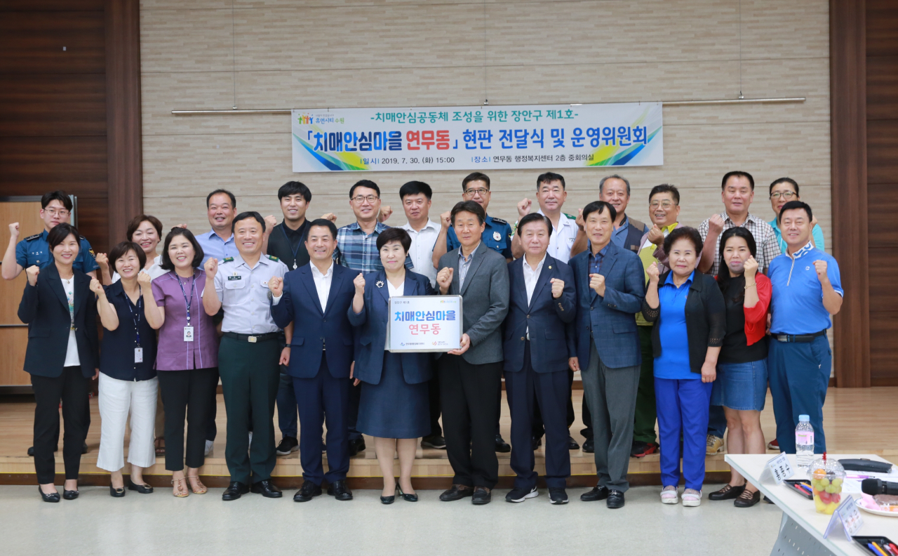 최혜옥 장안구보건소장(앞줄 왼쪽 여섯 번째), 전교영 연무동장(앞줄 왼쪽 일곱 번째)을 비롯한 관계자들이 연무동 행정복지센터에서 치매안심마을 현판식을 연 뒤 다함께 기념촬영을 하고 있다.[수원시 제공]