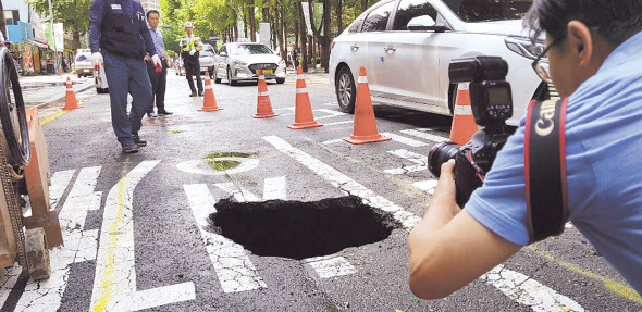 1일 내린 비로 청계천 1가 효령빌딩 앞에 약 1m 크기로 생긴 싱크홀을 사진 기자들이 촬영을 하고 있다. 중구는 하얀 포장으로 덮어 차량이 다니지 못하도록 임시 조치를 취했다.  정희조 기자/checho@heraldcorp.com