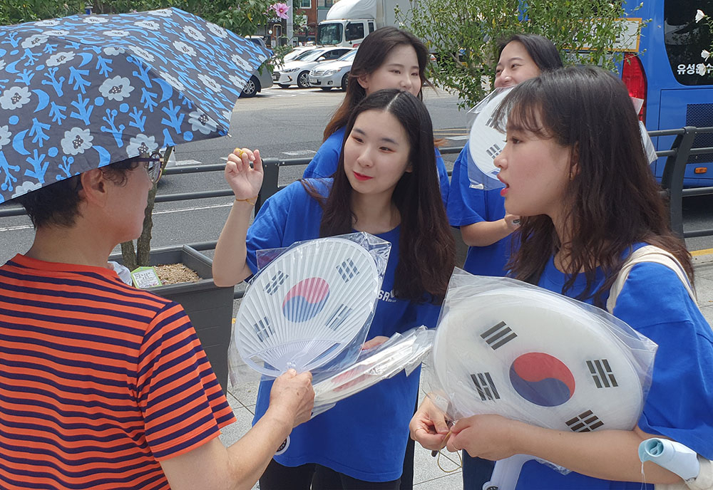 bhc치킨 해바라기 봉사단이 지난 14일 서울 서대문구에 위치한 독립문을 찾아 시민들에게 태극기 부채를 건네고 있다. [bhc치킨 제공]