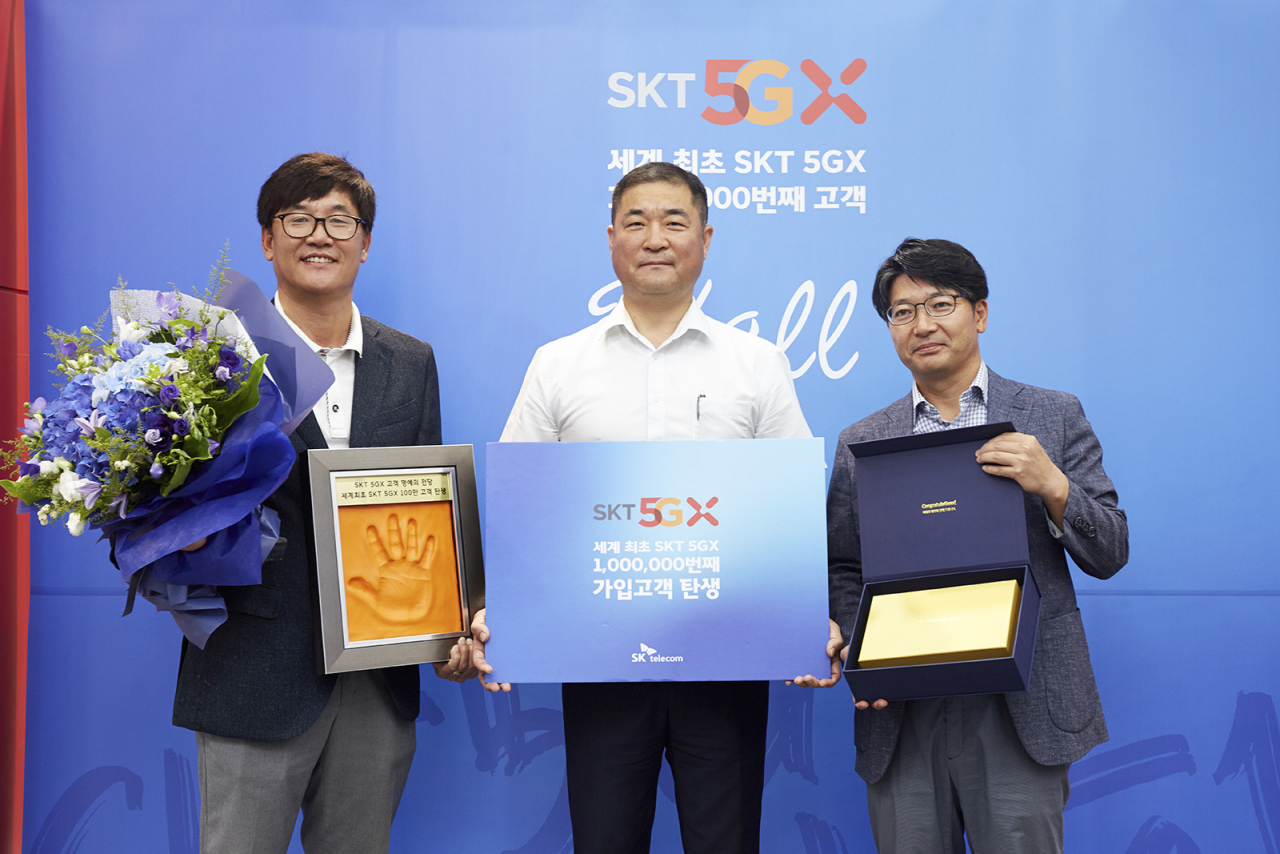 SK텔레콤은 세계 최초 5G 100만 명 돌파를 기념해 100만 번째 5G 고객을 찾아 22일 부산시 해운대구 T월드 대리점에서 축하 행사를 펼쳤다. (사진 왼쪽부터) SK텔레콤 김성수 영업본부장, 100만번째 고객 이상국 씨, SK텔레콤 임봉호 부산마케팅본부장이 핸드 프린팅과 경품을 들고 포즈를 취하고 있다.[SKT 제공]