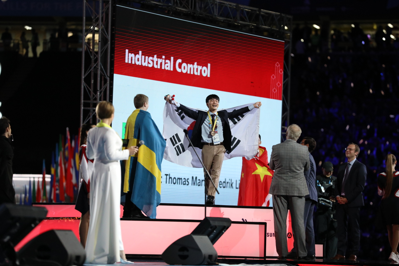 Yang Su-min (center) of Samsung Heavy Industries who won the gold medal in the Industrial Control category stands on the podium holding the South Korean national flag during the closing ceremony of the 45th WorldSkills Competition at Kazan Arena Stadium on Tuesday evening. (Human Resources Development Service of Korea)