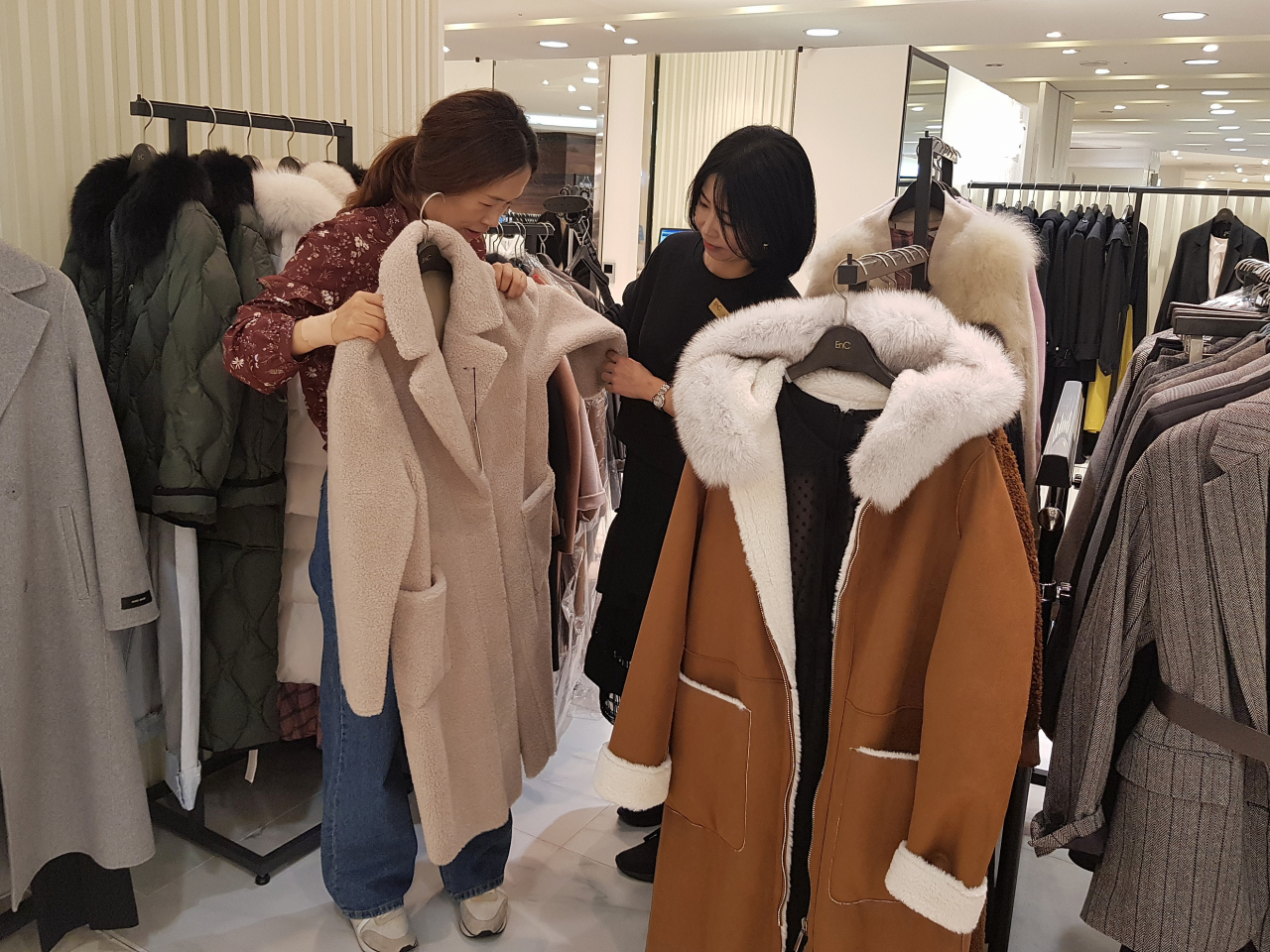 롯데백화점 부산본점 2층 E&C 매장에 겨울 신상품 할인행사를 펼쳐 고객이 코트를 살펴보고 있는 모습(좌)과 5층 아이터 매장에 진열된 후리스 점퍼를 둘러보고 있는 모습(우)