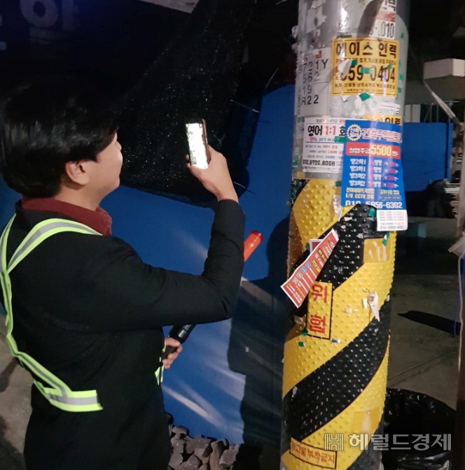 꾸러기수비대 대원이 고장난 가로등을 신고하기 위해 전주에 붙은 가로등 번호를 휴대폰으로 찍고 있다. [관악구 제공]