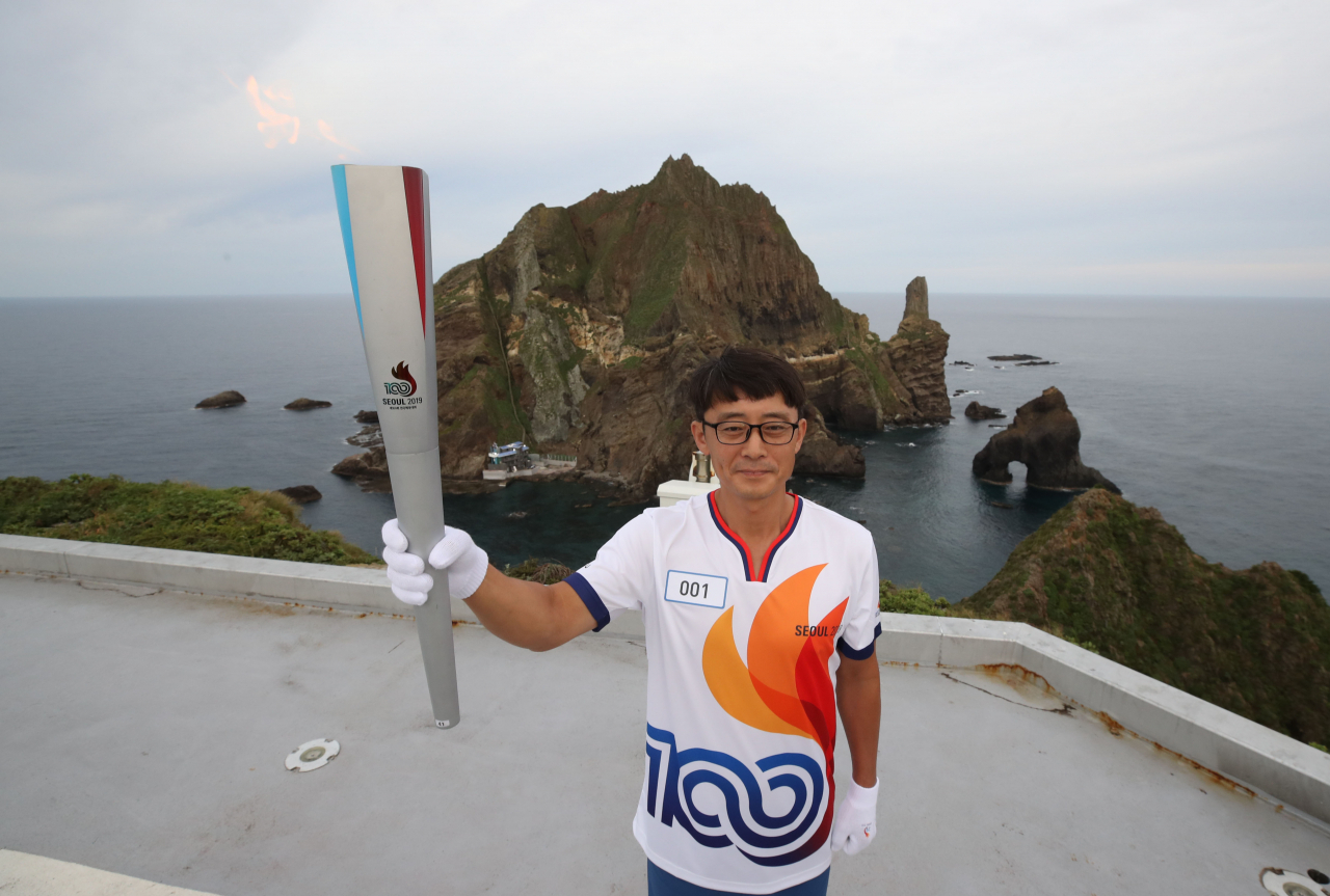 26일 오전 경북 울릉군 독도 경비대 헬기장에서 열린 제100회 전국체전 성화 채화 행사에서 허원석 독도경비대장이 성화를 봉송하고 있다. 울릉도를 거쳐 서울에 도착하는 ‘독도 성화’는 강화도 마니산 참성단, 임진각, 마라도 등에서 채화한 성화와 함께 오는 29일 서울광장에서 합화된다. [연합]