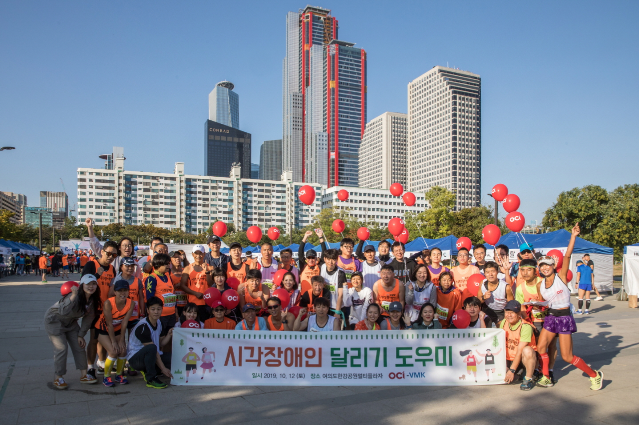 지난 12일 서울 여의도한강공원에서 열린 시각장애인 마라톤 대회에서 참가들과 OCI 임직원 봉사자들이 단체사진을 찍고 있다. [OCI 제공]
