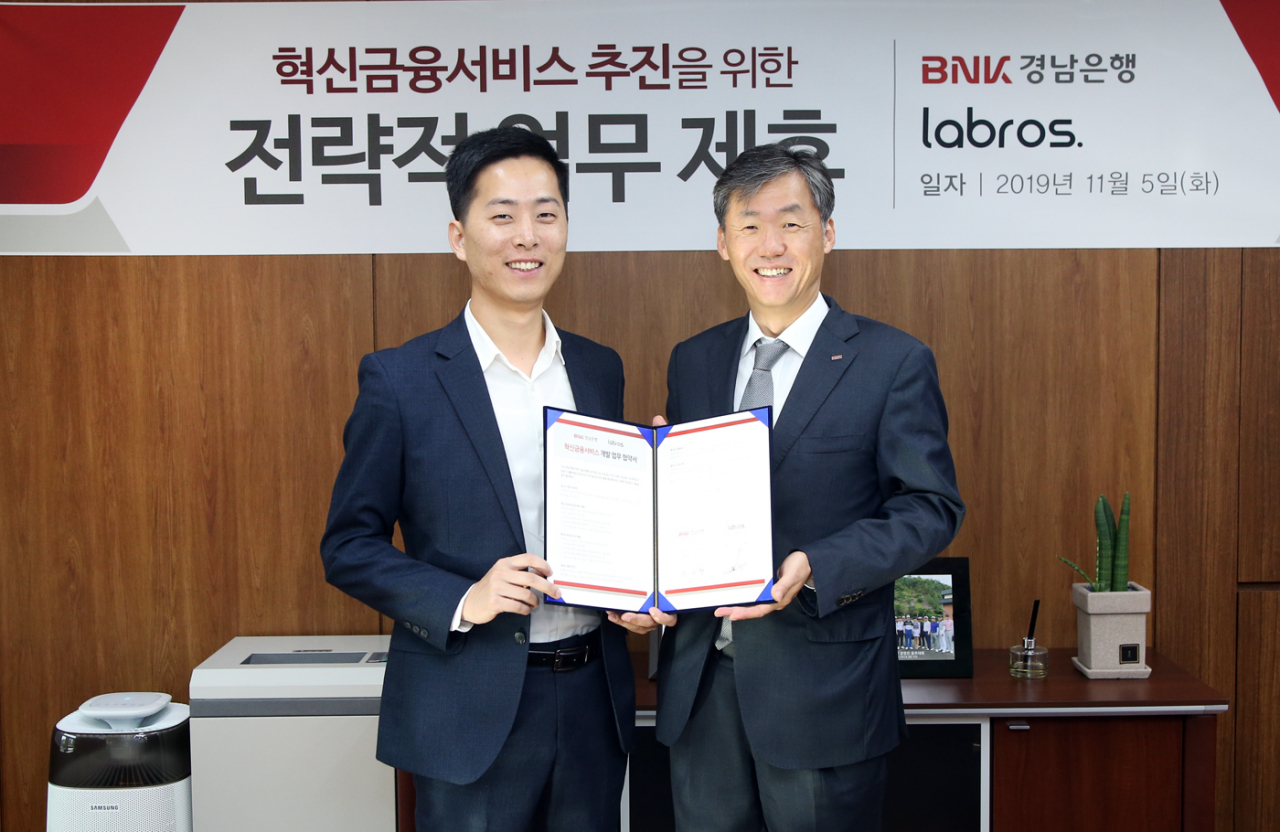 BNK경남은행 최우형 부행장보(사진 오른쪽)가 라브로스 주식회사 이창수 대표이사와 ‘모바일 외화 환전 혁신금융서비스 공동 개발 추진을 위한 업무 협약’을 체결하고 있다.