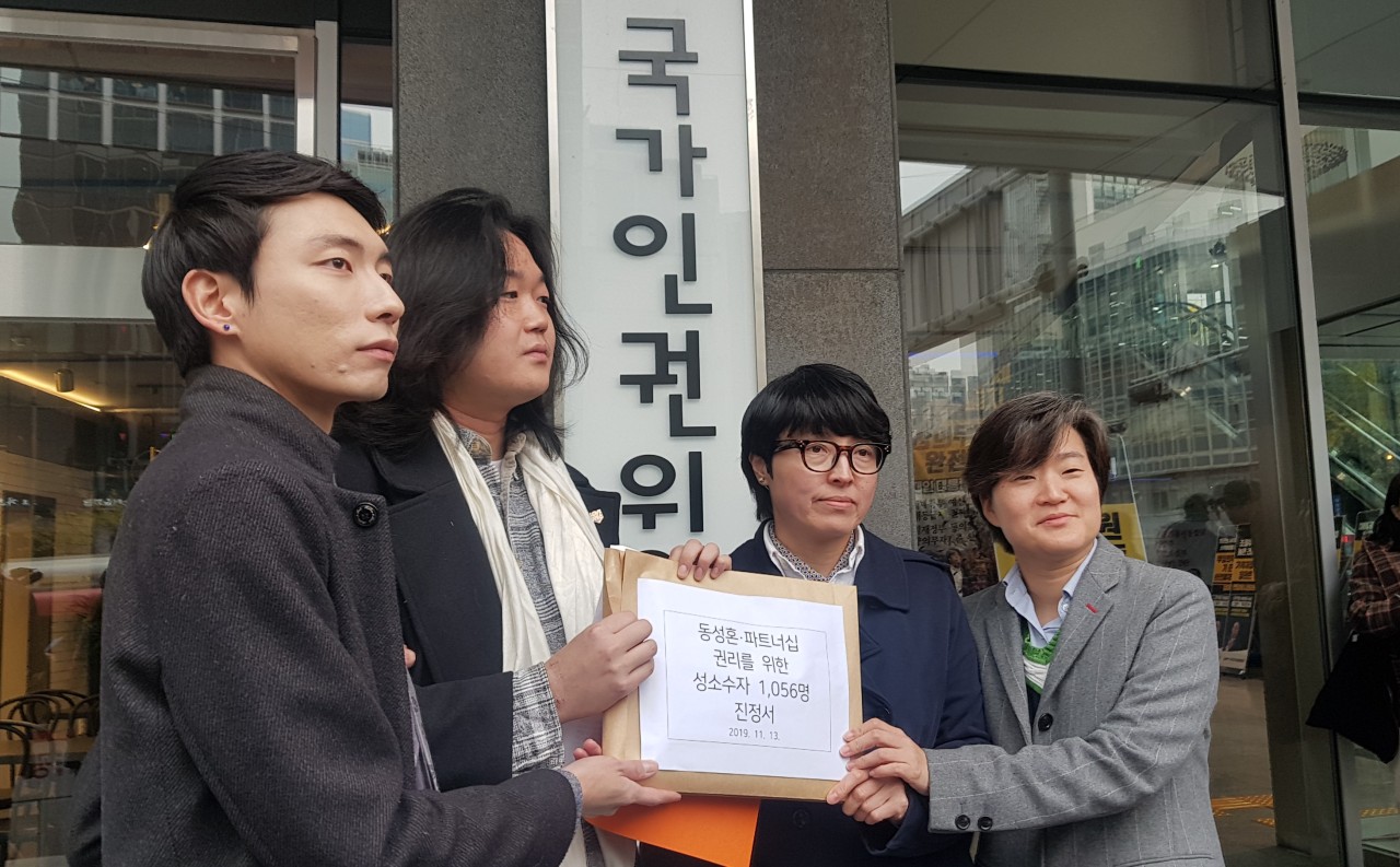 From left, Kim Yong-min, Kim's partner So Sung-uk, Yoon Hwa-young and Yoon's partner Chang Suh-yeon, hold up the petition document in front of the National Human Rights Commission of Korea building on Wednesday. (Choi Ji-won/ The Korea Herald)