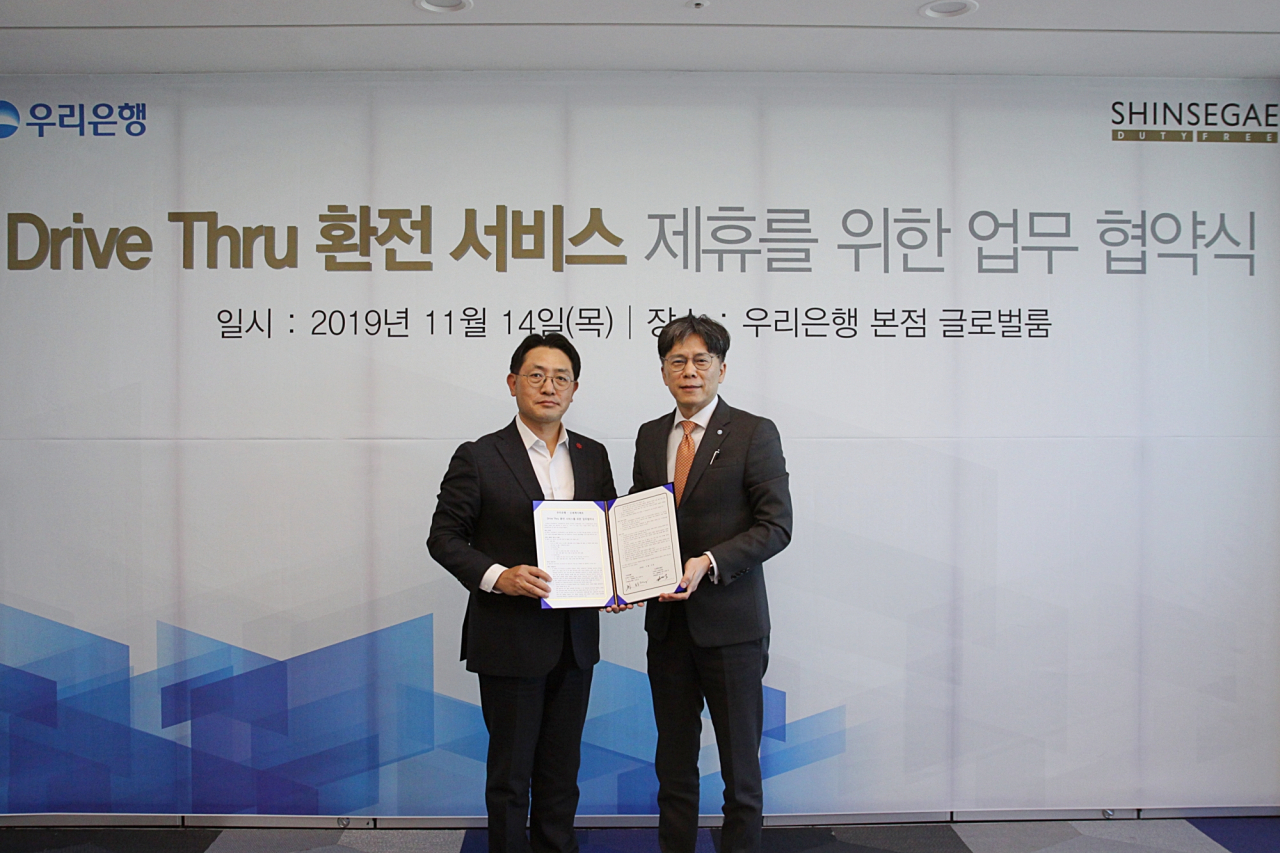 우리은행은 신세계면세점과 드라이브 스루 환전 제휴를 위한 업무 협약식을 14일 가졌다. 황원철 우리은행 디지털금융그룹장(오른쪽)과 문현규신세계면세점 마케팅 담당 상무가 기념촬영을 하고 있다.