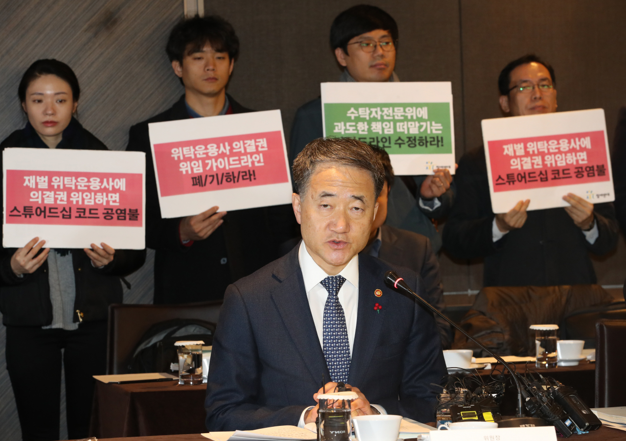 박능후 보건복지부 장관이 29일 오전 서울 중구 더플라자호텔에서 열린 제8차 국민연금 기금운용위원회 회의를 주재하고 있다. 뒤편에서는 참여연대 경제금융센터 관계자 등이 '수탁자책임에 관한 원칙(스튜어드십코드)' 가이드라인 재논의를 촉구하는 피켓을 들고 있다. [연합]