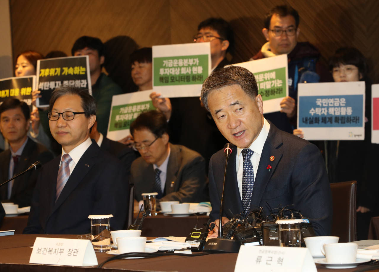 박능후 보건복지부 장관이 29일 오전 서울 중구 더플라자호텔에서 열린 제8차 국민연금 기금운용위원회 회의를 주재하고 있다. 뒤편에서는 참여연대 경제금융센터 관계자 등이 '수탁자책임에 관한 원칙(스튜어드십코드)' 가이드라인 재논의를 촉구하는 피켓을 들고 있다. [연합]