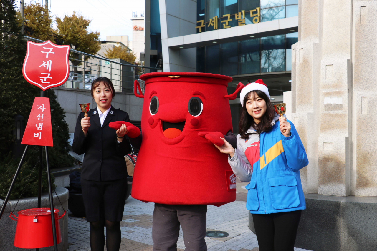 CJ대한통운이 연말 구세군의 자선모금 활동에 사용되는 물품 1000여 개의 무료배송을 후원한다. CJ대한통운 직원(오른쪽)과 구세군 직원(왼쪽)이 구세군 캐릭터 ‘따끈이’와 함께 기념촬영을 하고 있다. [CJ대한통운 제공]