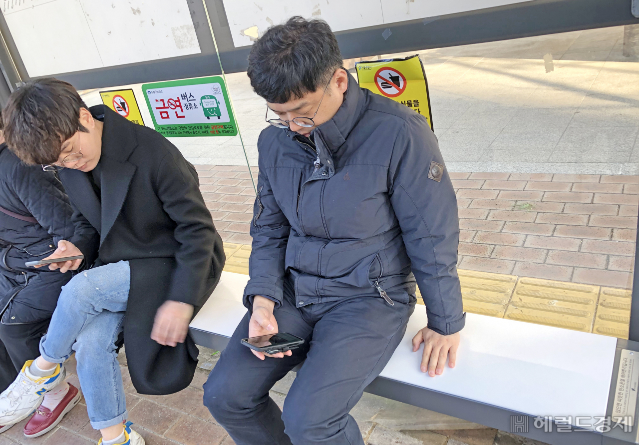 시민들이 도봉구청 버스정류소에 설치된 한파 가림막 추위녹이소 안의 IoT탄소온열의자에 앉아 버스를 기다리고 있다.