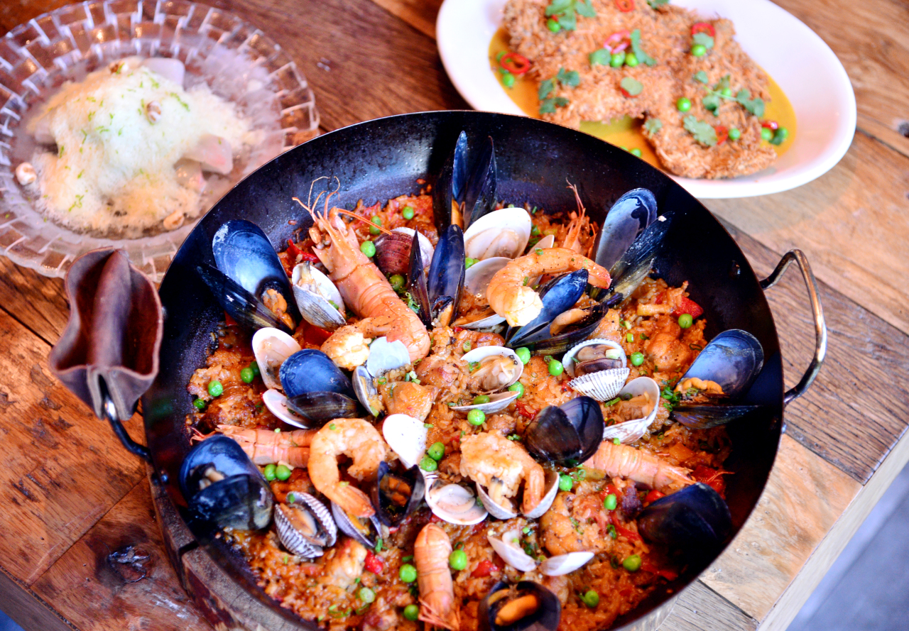 Sigolo’s paella mixta (front) features housemade chorizo, seasoned chicken, clams, mussels, shrimp, red-banded lobster and crisp, crunchy socarrat. Sigolo’s lamb katsu (right, back) draws inspiration from Japanese tonkatsu and Thai curry while the halibut ceviche (left, back) sends a nod to Korean “bingsu.” (Photo credit: Park Hyun-koo/The Korea Herald)
