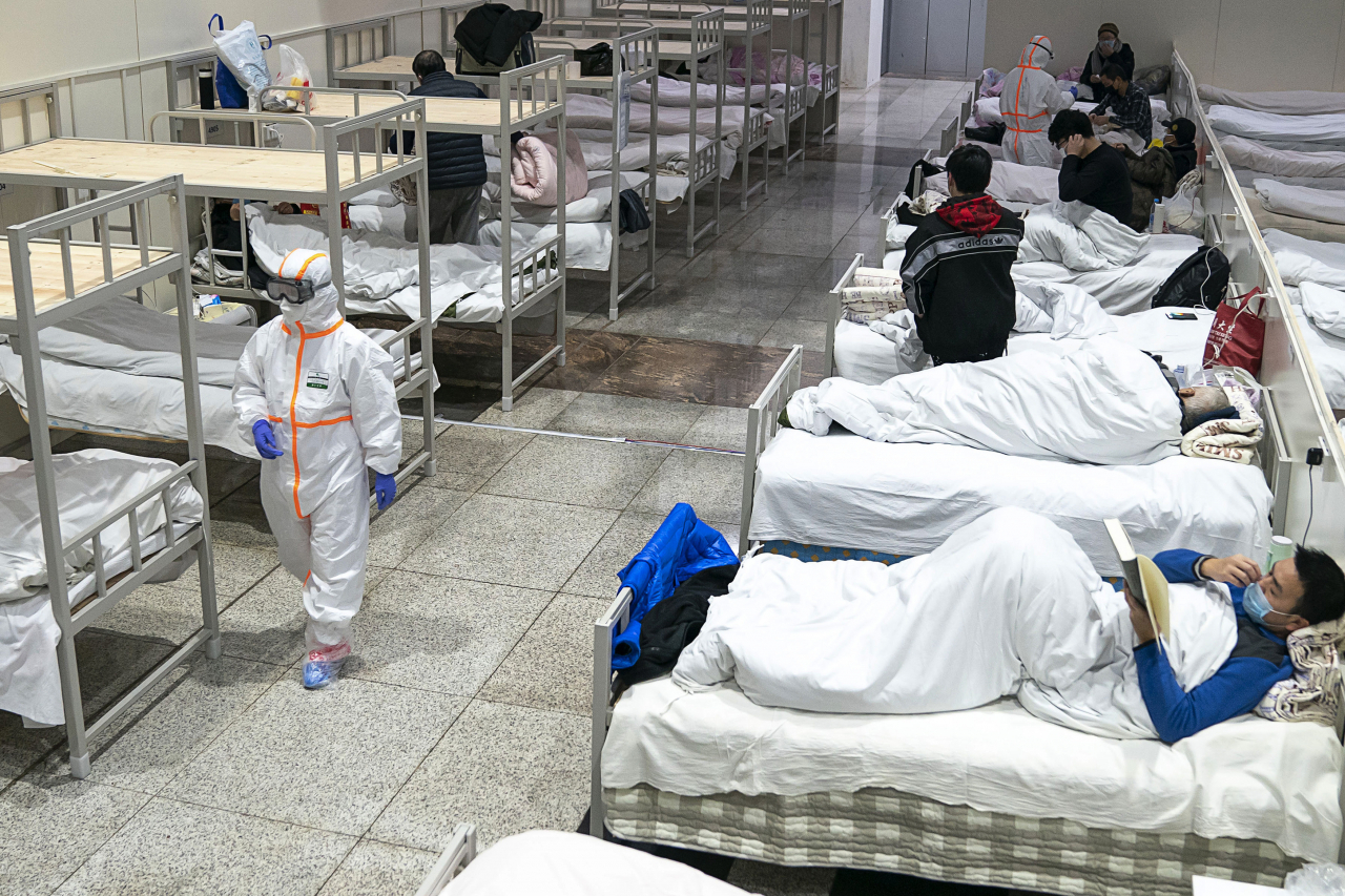 지난 5일 중국 후베이성 우한의 한 대형 전시장을 개조한 임시병원에서 보호복을 입은 의료진이 신종 코로나바이러스 감염증 환자들 옆을 지나가고 있다. [연합]