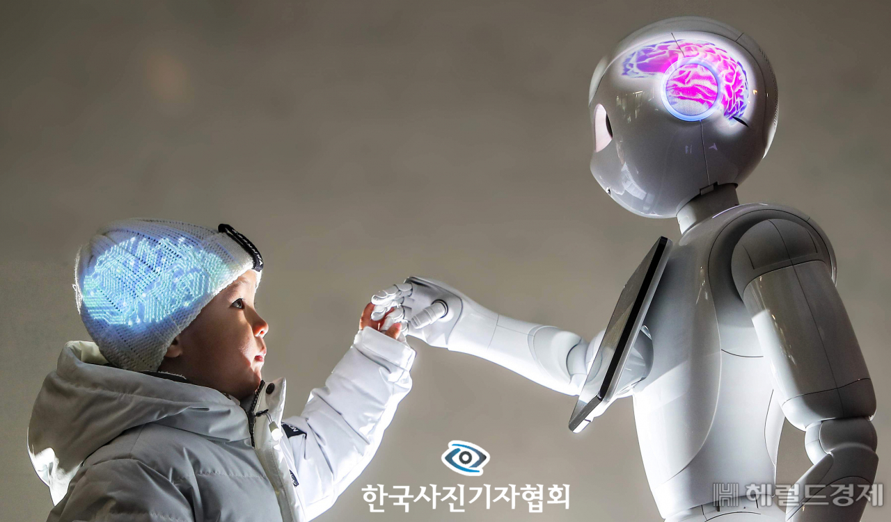 〈56회 한국보도사진상 - 최우수상〉 “너처럼 똑똑하고 단단해지고 싶어.” 아이는 마주 선 로봇의 손을 꼬옥 잡으며 새해 소망을 전했다. “왜 나처럼 되고 싶어?” 로봇이 물었다. “어려운 이웃을 돕고, 남을 괴롭히는 사람들을 혼내주는 훌륭한 사람이 될 수 있잖아. 네 소원은 뭐니?” 아이가 물었다. “너처럼 따뜻한 마음을 갖고 싶어.” 아이의 머리에는 로봇의 전자회로를, 로봇의 머리에는 인간의 뇌를 프로젝트로 투사해 촬영. 〈박영대, 양회성기자/ 동아일보/ 한국사진기자협회 - 무단전재 재배포금지〉