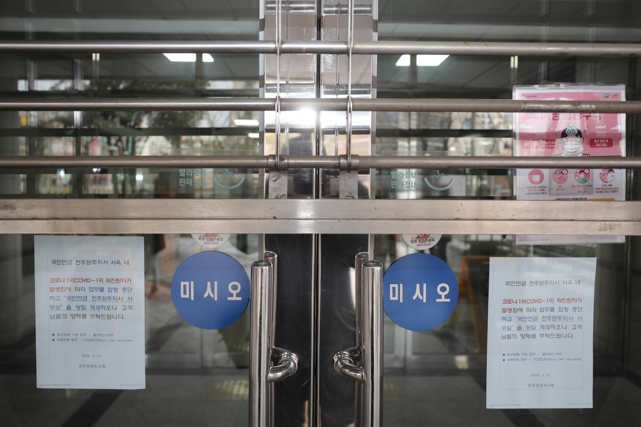 21일 오전 신종 코로나바이러스 감염증(코로나19) 확진자가 근무하던 사무실이 있는 전북 전주시 완산구 국민연금공단 전주지사 건물이 임시 폐쇄된 가운데 출입문에 출입 자제 안내문이 붙어 있다. 연합뉴스