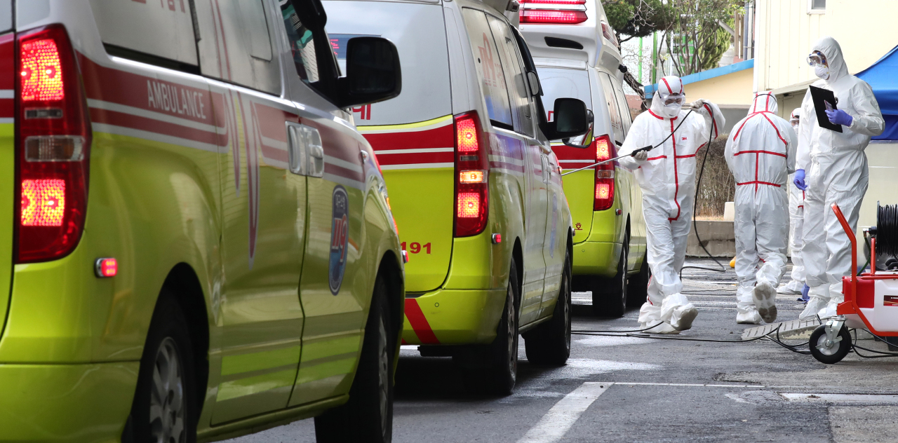 Health workers in protective suits stand next to a line of ambulances at a hospital in central Daegu. (Yonhap)
