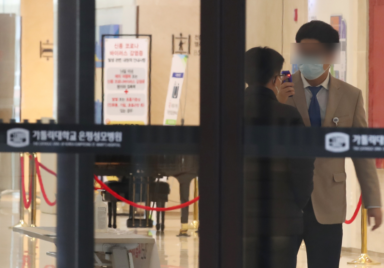 26일 서울 은평성모병원 로비에서 보안 요원이 병원 내부 출입자의 체온을 확인하고 있다. 전날 서울 은평성모병원 관련 신종 코로나 바이러스 감염증 확진자가 1명 추가되면서 모두 5명으로 늘었다. 서울시는 2월 1일부터 은평성모병원을 방문했던 사람 중 발열, 기침 등 호흡기 증상이 있는 방문객은 마스크를 착용한 후 선별 진료소를 방문해달라고 당부하고 휴대전화 안전 안내 문자 메시지로 이런 내용을 공지했다. 연합뉴스