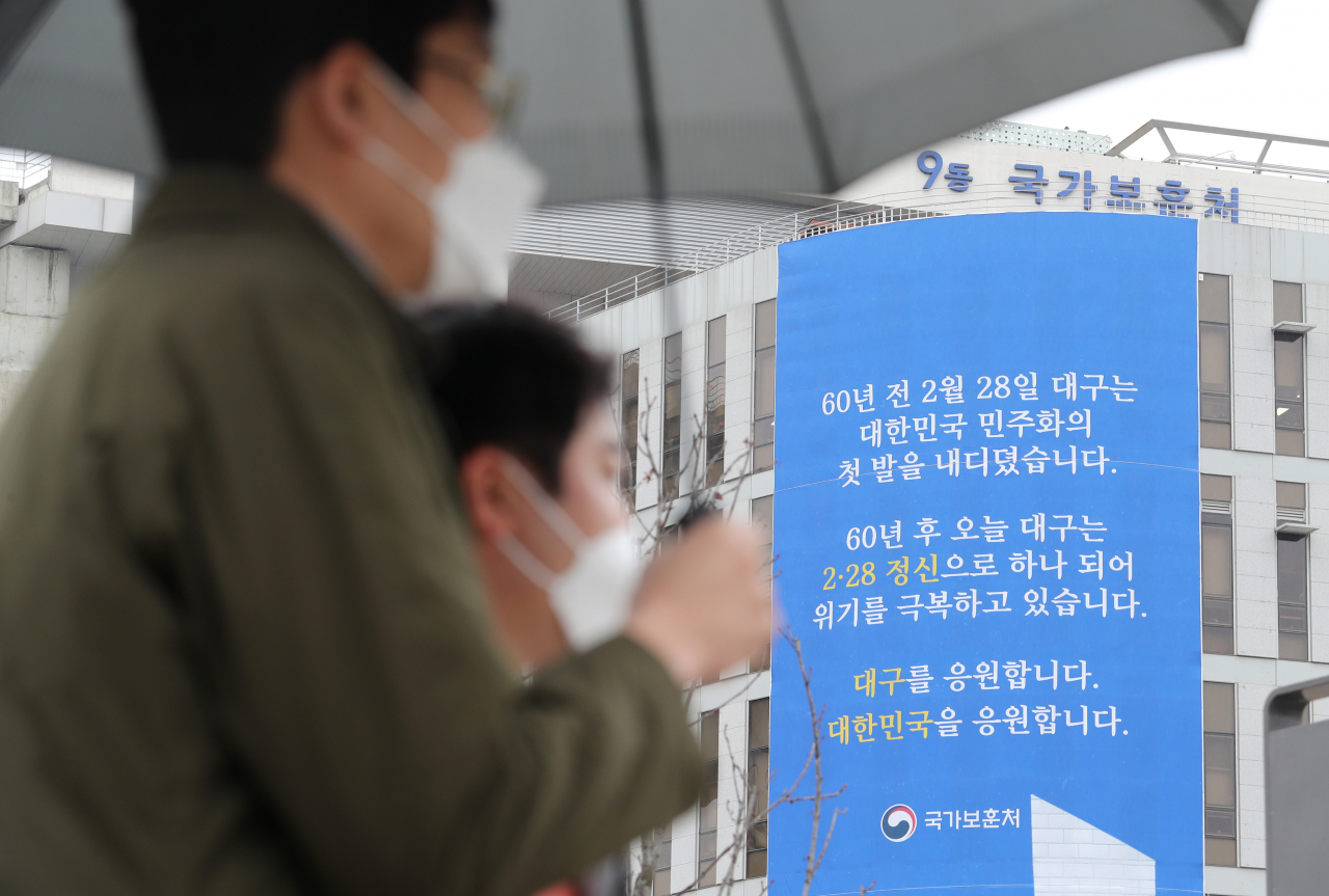 비가 내리는 28일 오전 세종시 정부세종청사 국가보훈처에 코로나19로 고통을 겪고 있는 대구시민을 응원하는 글이 담긴 현수막 앞으로 시민들이 지나가고 있다. 연합뉴스