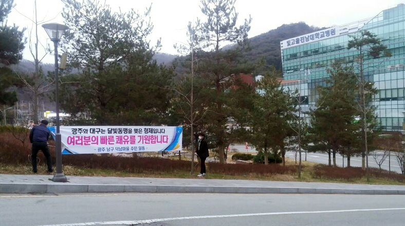 지난 3일 오후 광주 남구 빛고을 전남대병원 앞에서 인근 마을인 덕남마을 주민들이 이곳으로 이송돼 치료를 받게 될 코로나19 대구 확진자들의 쾌유를 기원하는 현수막을 부착하고 있다. [연합]