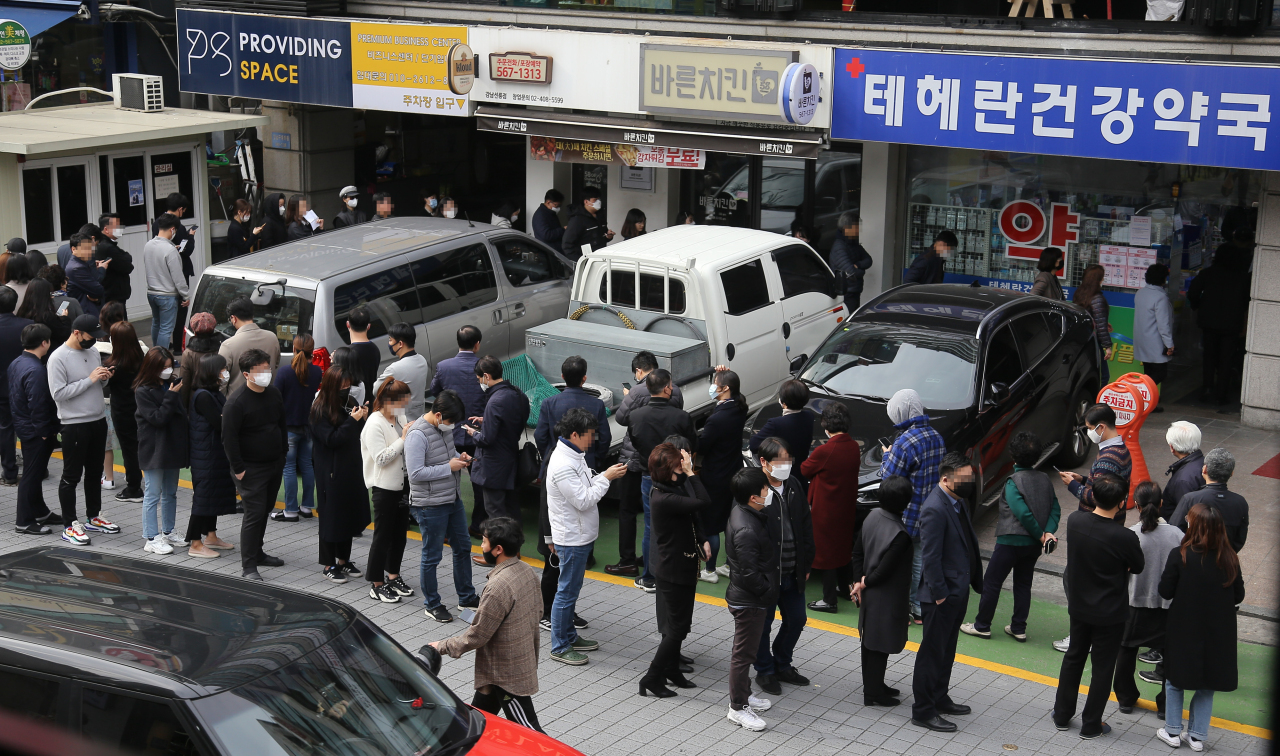 People line up to buy face masks, considered essential as a precaution against the new coronavirus, in front of a pharmacy in central Seoul on Monday, as the nation introduces a new distribution system to ease the acute supply shortage. Yonhap　