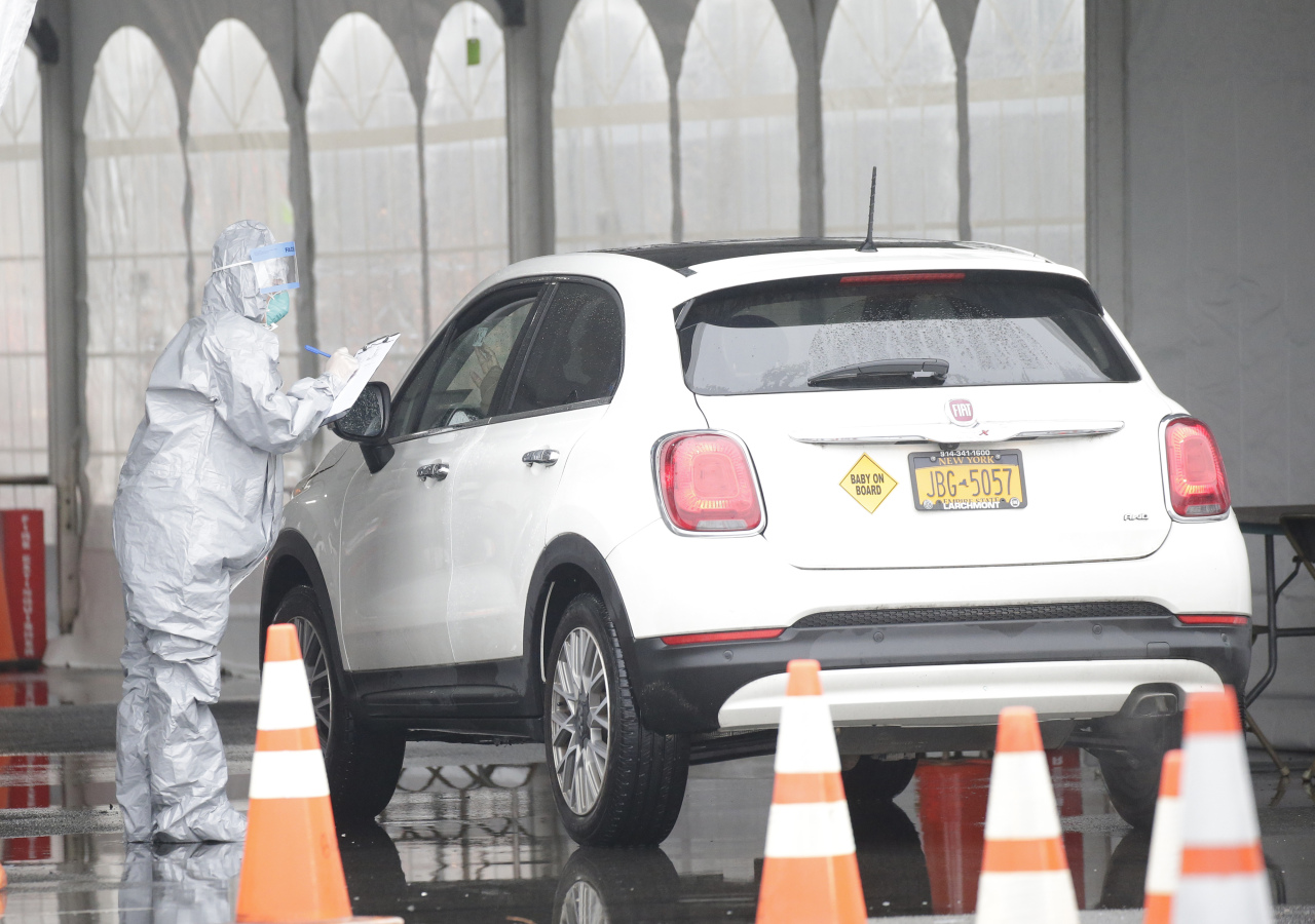 Workers in protective suits check ID of possible patients when they arrive by car at NY State's first drive through virus mobile testing center at Glen Island Park in New Rochelle on Friday. (UPI-Yonhap)