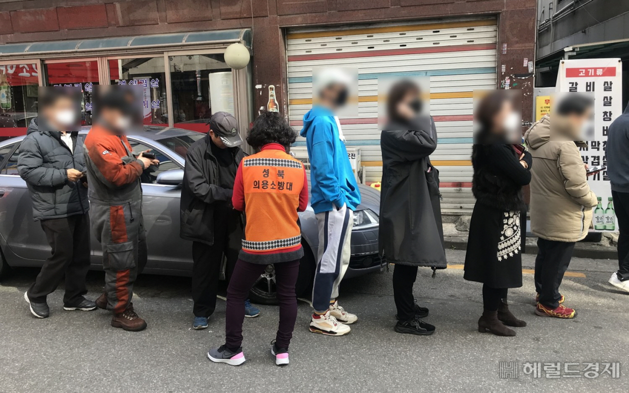 의용소방대원이 공적마스크 구입을 위해 길게 줄서 있는 시민들을 대상으로 신분을 확인하고 있다. [성북구]