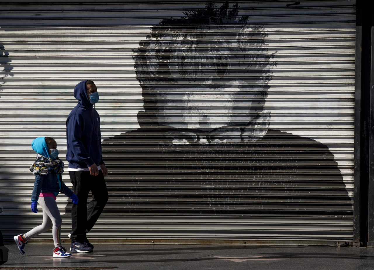 미 로스앤젤레스에서 마스크를 쓴 시민들이 거리를 지나고 있다 [AP]