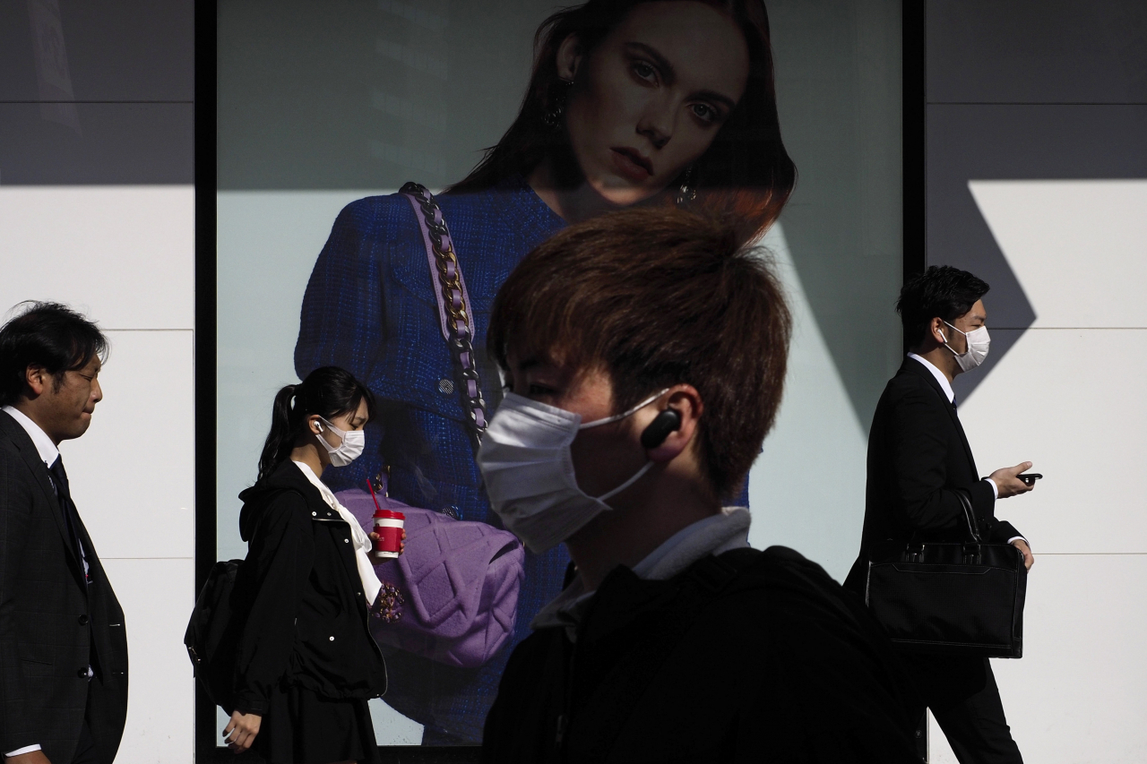 일본 닛케이평균주가가 26일 도쿄도(東京都)의 코로나19 확진자 급증으로 도시 봉쇄 우려가 높아지면서 4% 이상 급락했다. 사진은 이날 출근길 시민들이 마스크를 쓴채 도쿄 신주쿠역 앞을 지나고 있다. 외곽의 한 광고를 지나가고 있다. 아베 신조(安倍晋三) 총리는 코로나19 확진자의 폭발적인 증가 등 예기치 못한 사태에 대비하기 위해 특별조치법에 근거한 정부 대책본부 설치하기로 했다. [AP]