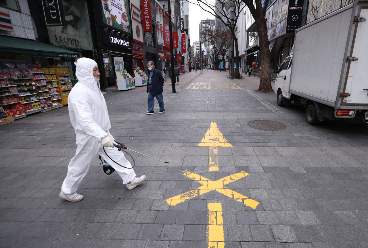 An official from the Jung-gu District Office takes a disinfectant equipment across an empty street in Myeongdong, central Seoul. (Yonhap)