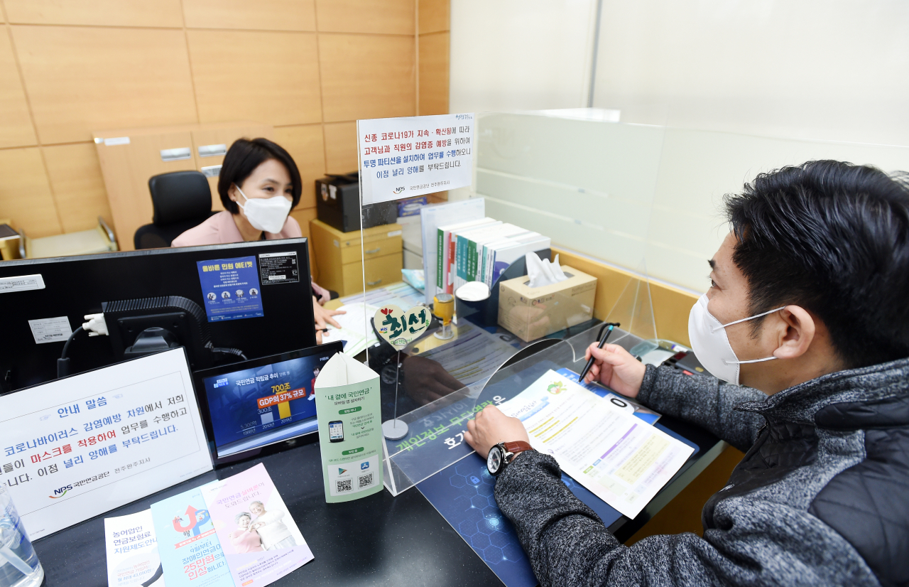 국민연금공단이 코로나19 극복에 전사적으로 대응하고 있는 가운데 전주완주지사에서 직원이 마스크를 쓴 채 투명 칸막이(파티션)이 설치된 창구에서 고객상담 업무를 수행하고 있다. [국민연금공단 제공]　