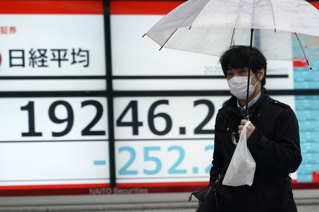 한 남성이 13일 마스크를 착용하고 우산을 든 채 니케이지수가 표시된 전광판 앞을 지나고 있다. [AP]