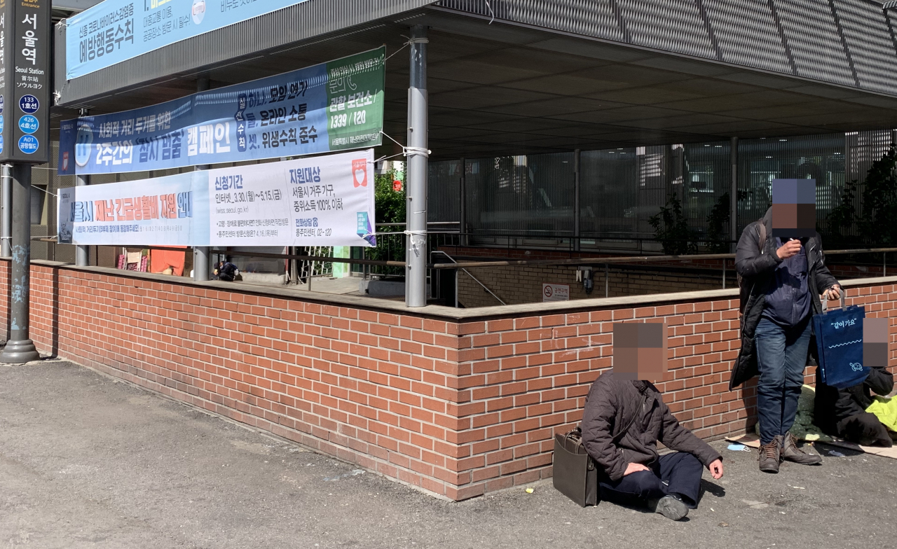 지난 23일 오전 서울 용산구 지하철 서울역 2번 출구 앞. 노숙인들이 펄럭이는 ‘서울시 재난긴급생활비’ 현수막 밑에서 박스를 깔고 앉아 있다. 신주희 기자/joohee@heraldcorp.com