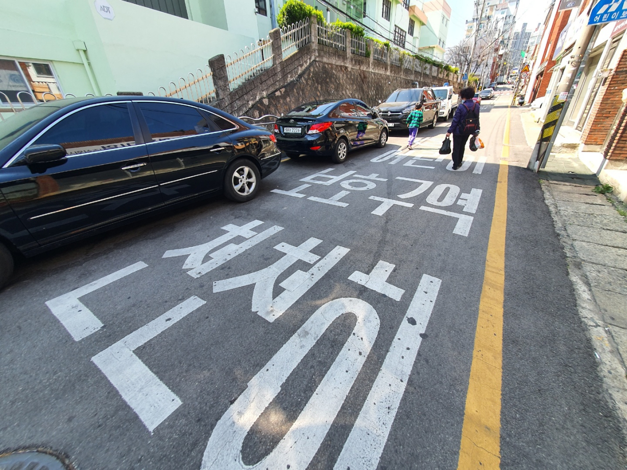 ‘민식이법’ 시행 첫날인 지난달 25일 부산 동래구 한 초등학교에 불법 주차된 차량 옆으로 한 어린이가 아찔한 보행을 하고 있다. [연합]