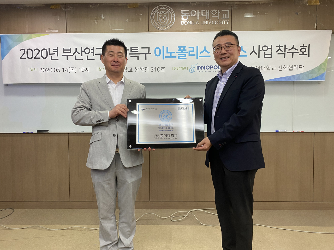 부산특구본부 오영환 본부장이 5월 14일 동아대에서 김재일 이노폴리스캠퍼스 사업 단장에게 이노폴리스캠퍼스 현판을 전달하고 있다.
