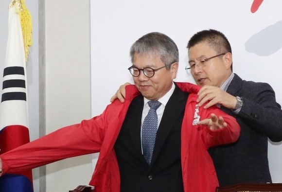김용하 순천향대 IT금융경영학과 교수가 지난해 10월31일 국회에서 열린 ‘제1차 영입인재 환영식’에서 황교안 당시 자유한국당 대표로부터 점퍼를 받고 있다. [연합]